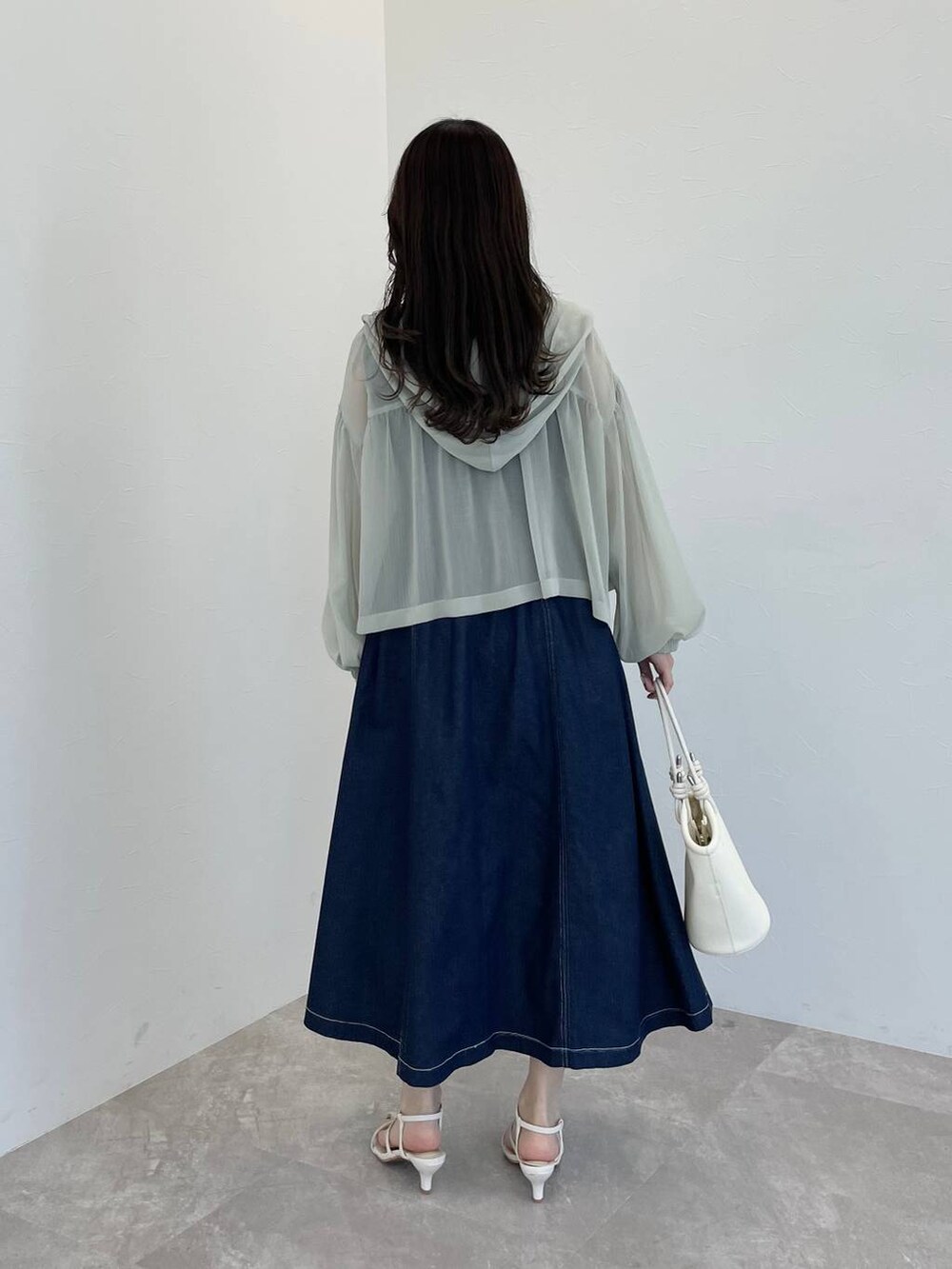 ホワイト系のハンドバッグ、グリーン系のパーカー、ブルー系のジャンパースカートを着用したレディースの春コーディネートの2枚目の写真