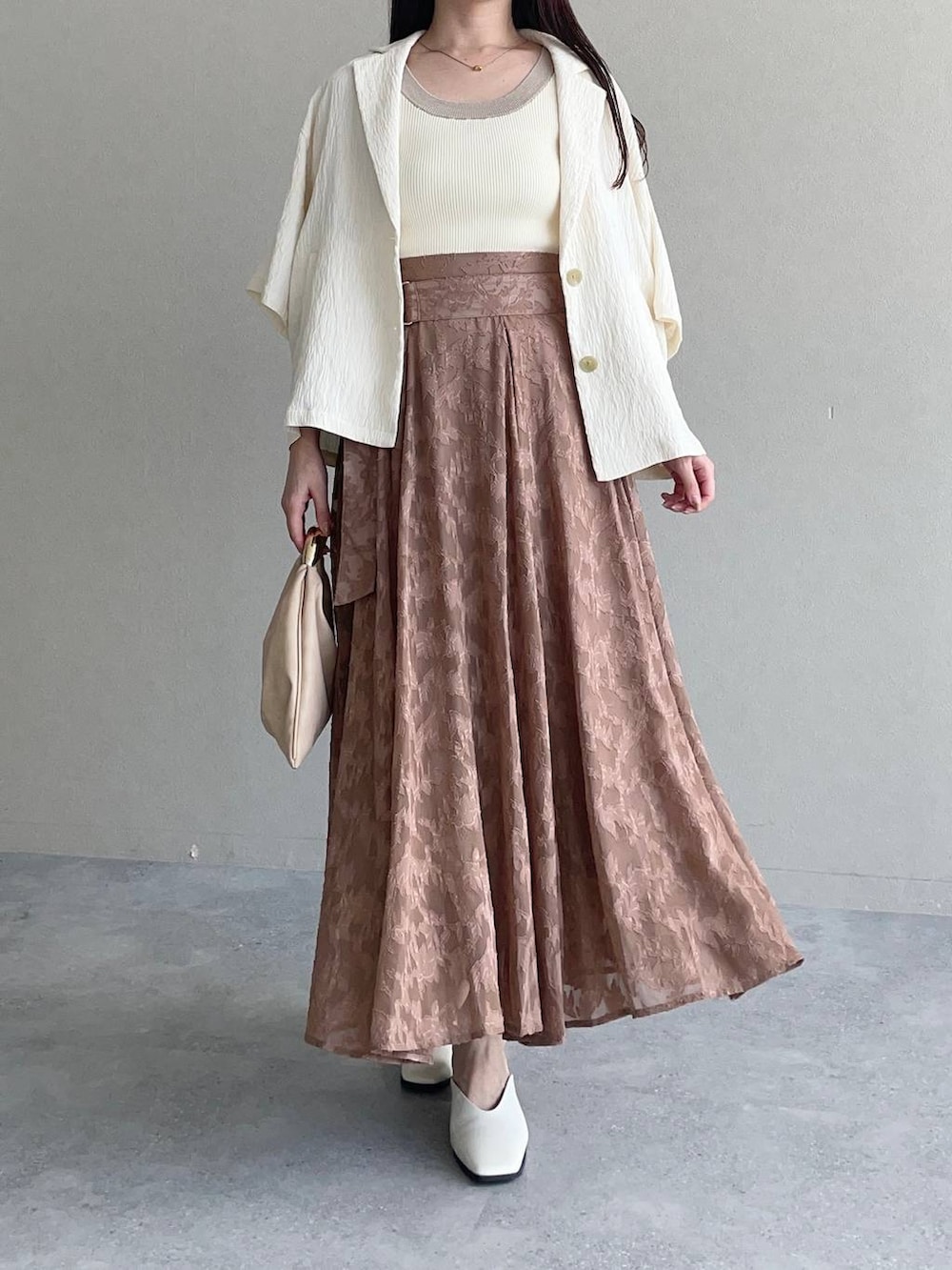 ホワイト系のテーラードジャケット、ベージュ系のハンドバッグ、ホワイト系のタンクトップを着用したレディースの秋コーディネートの3枚目の写真