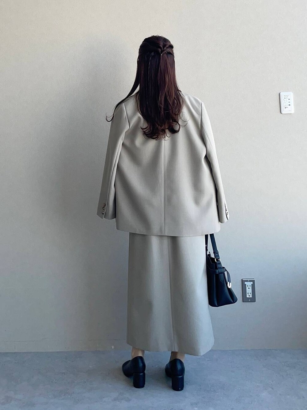 ブラック系のショルダーバッグ、ベージュ系のテーラードジャケット、ベージュ系のジャンパースカートを着用したレディースの冬コーディネートの2枚目の写真