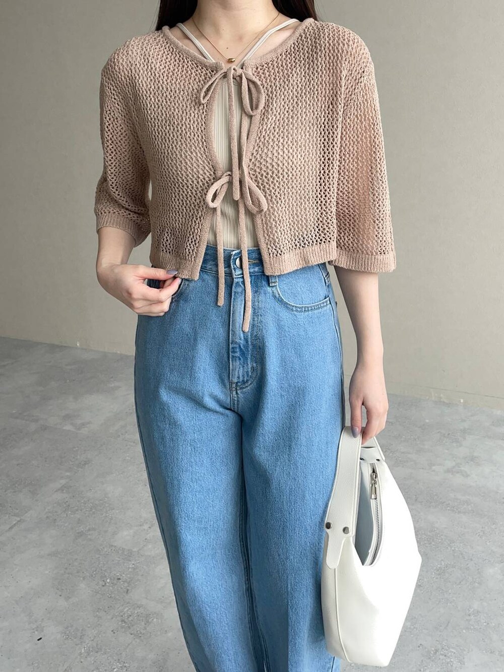 ブルー系のデニムパンツ、ベージュ系のカーディガン/ボレロ、ホワイト系のショルダーバッグを着用したレディースの春コーディネートの3枚目の写真