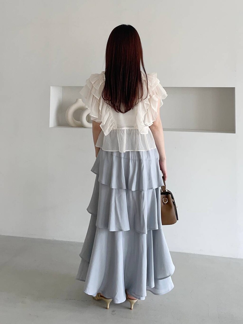 グレー系のスカート、ホワイト系のシャツ/ブラウス、ゴールド系のパンプスを着用したレディースの夏コーディネートの2枚目の写真