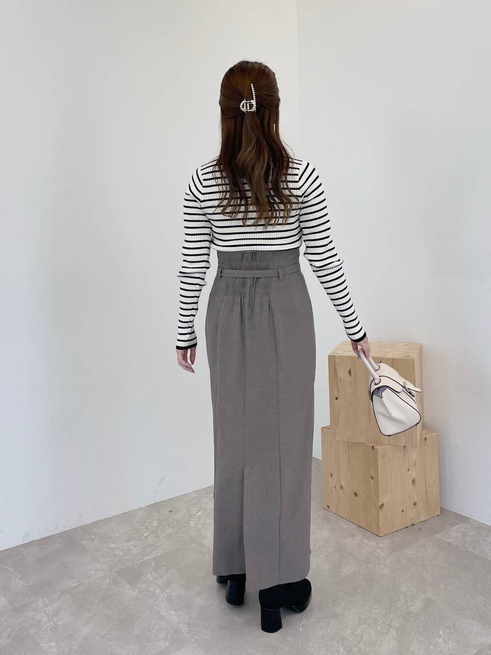 ブラウン系のスカート、ホワイト系のハンドバッグ、ブラック系のブーツを着用したレディースの秋コーディネートの2枚目の写真