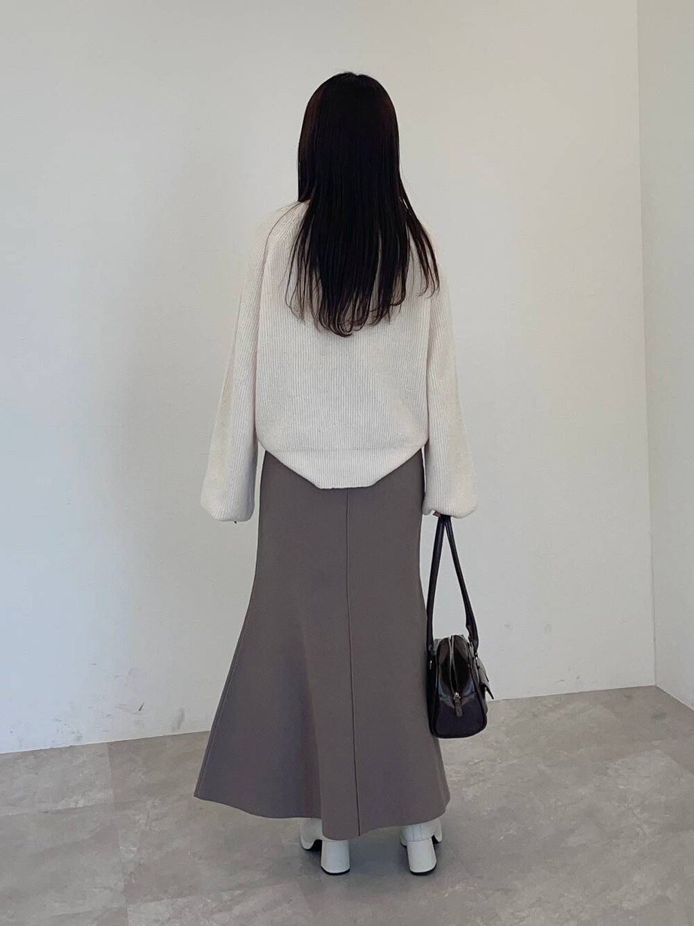 ホワイト系のブーツ、ホワイト系のニット/セーター、ブラウン系のハンドバッグを着用したレディースの冬コーディネートの2枚目の写真