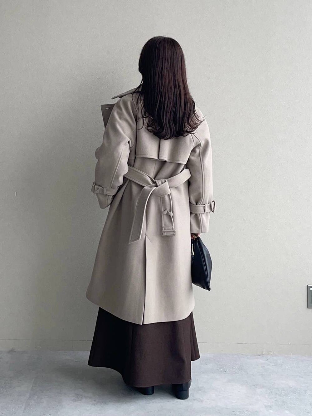 ベージュ系のチェスターコート、ブラック系のハンドバッグ、ブラウン系のスカートを着用したレディースの秋コーディネートの2枚目の写真