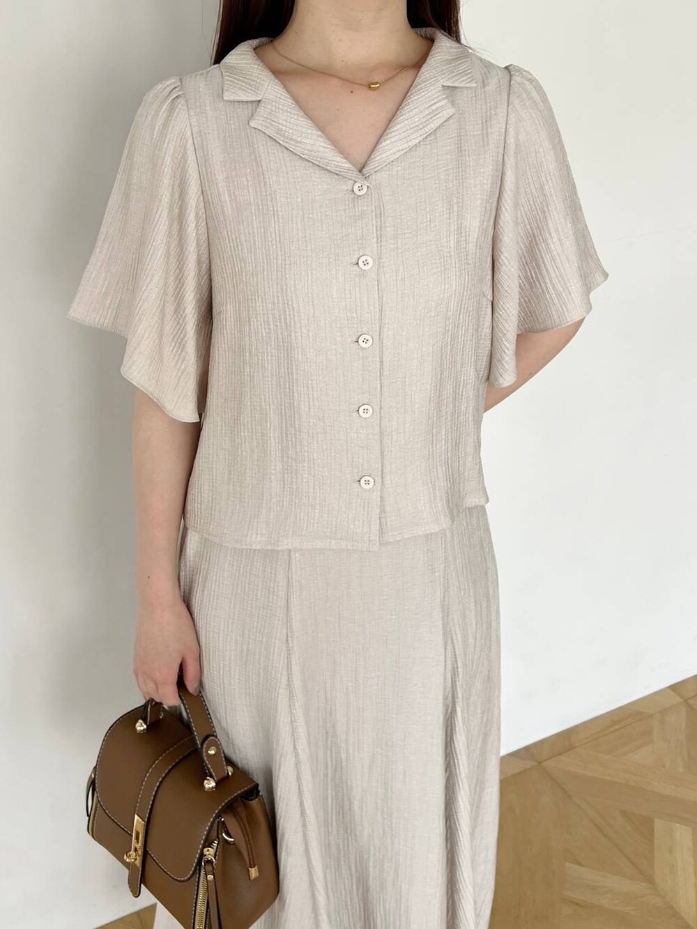 ゴールド系のパンプス、ブラウン系のショルダーバッグ、ベージュ系のスカートを着用したレディースの夏コーディネートの3枚目の写真