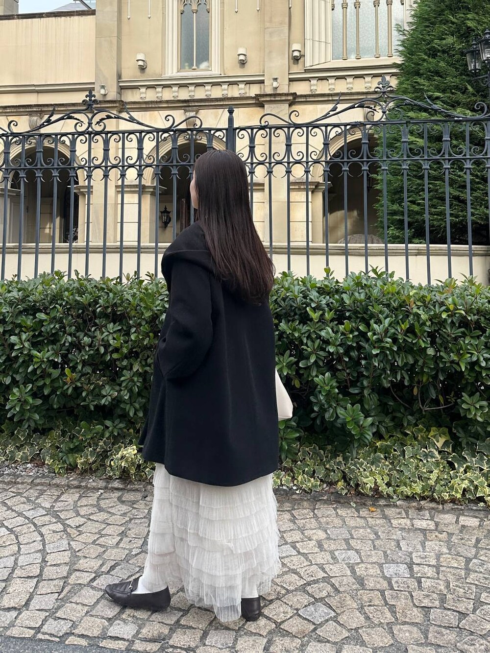 ブラック系のノーカラーコート、ホワイト系のスカートを着用したレディースの冬コーディネートの4枚目の写真