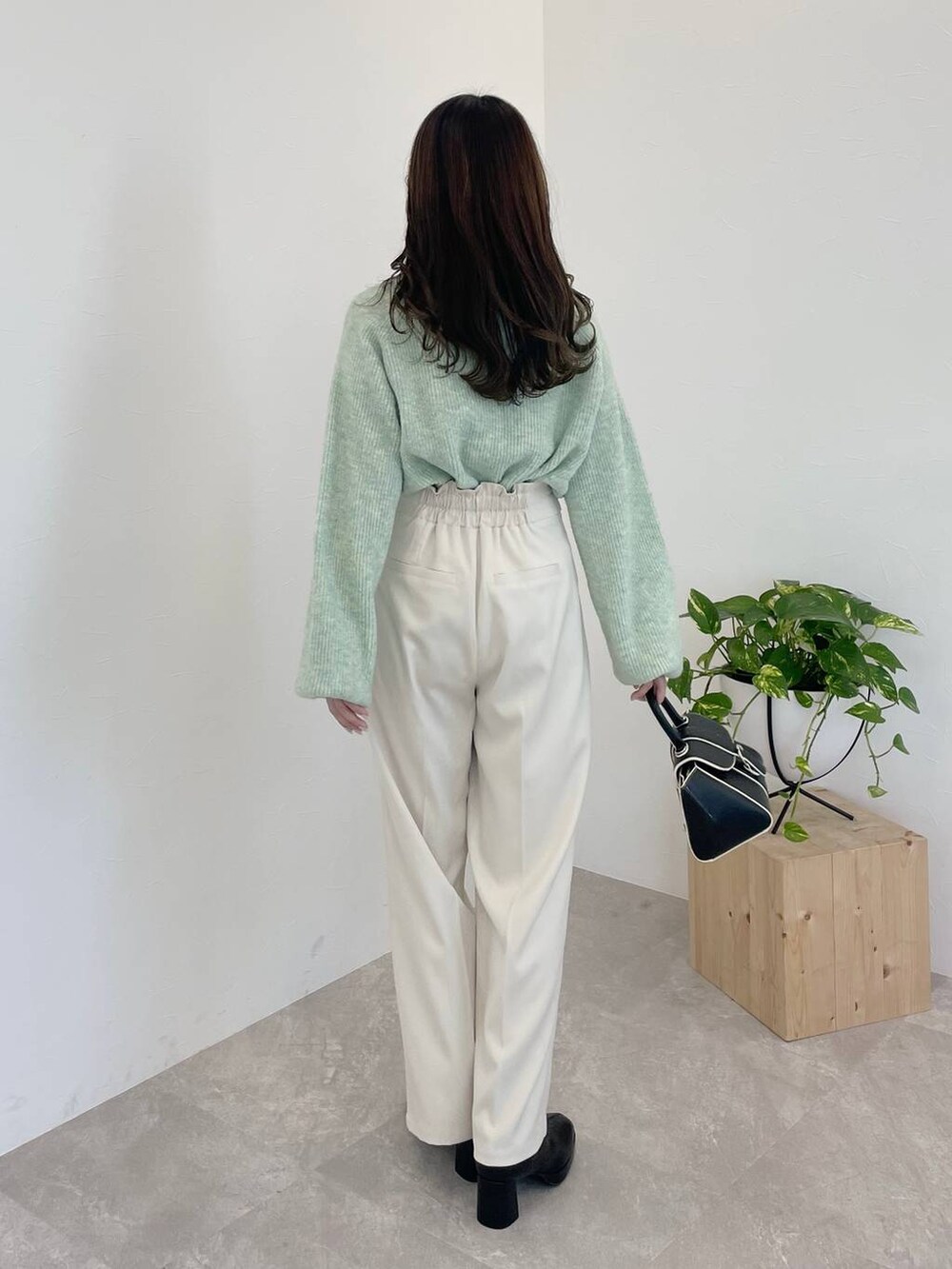 グリーン系のニット/セーター、ブラック系のハンドバッグ、ブラック系のブーツを着用したレディースの冬コーディネートの2枚目の写真