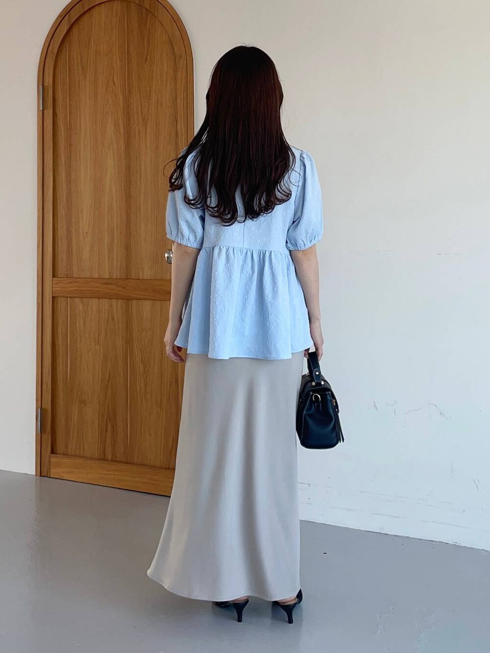 ベージュ系のスカート、ブラック系のパンプス、ブラック系のショルダーバッグを着用したレディースの夏コーディネートの2枚目の写真