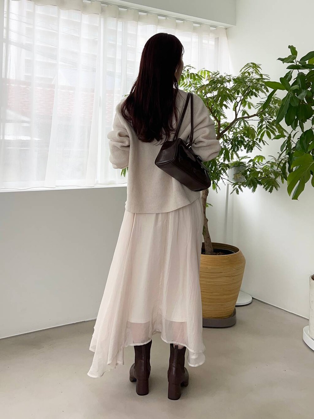 ブラウン系のブーツ、ホワイト系のニット/セーター、ブラウン系のハンドバッグを着用したレディースの冬コーディネートの2枚目の写真