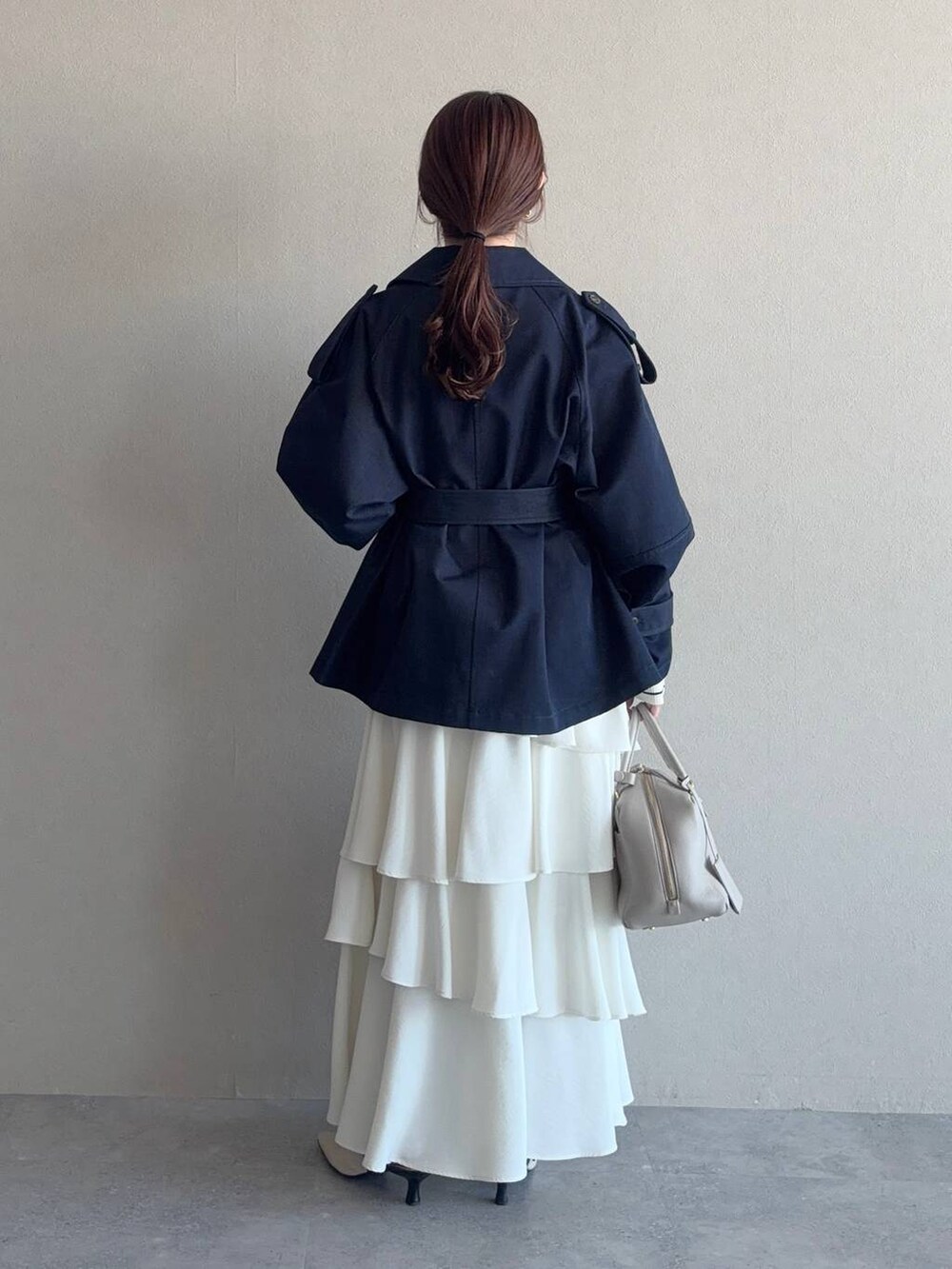 ベージュ系のハンドバッグ、ホワイト系のサンダル、ブルー系のトレンチコートを着用したレディースの冬コーディネートの2枚目の写真