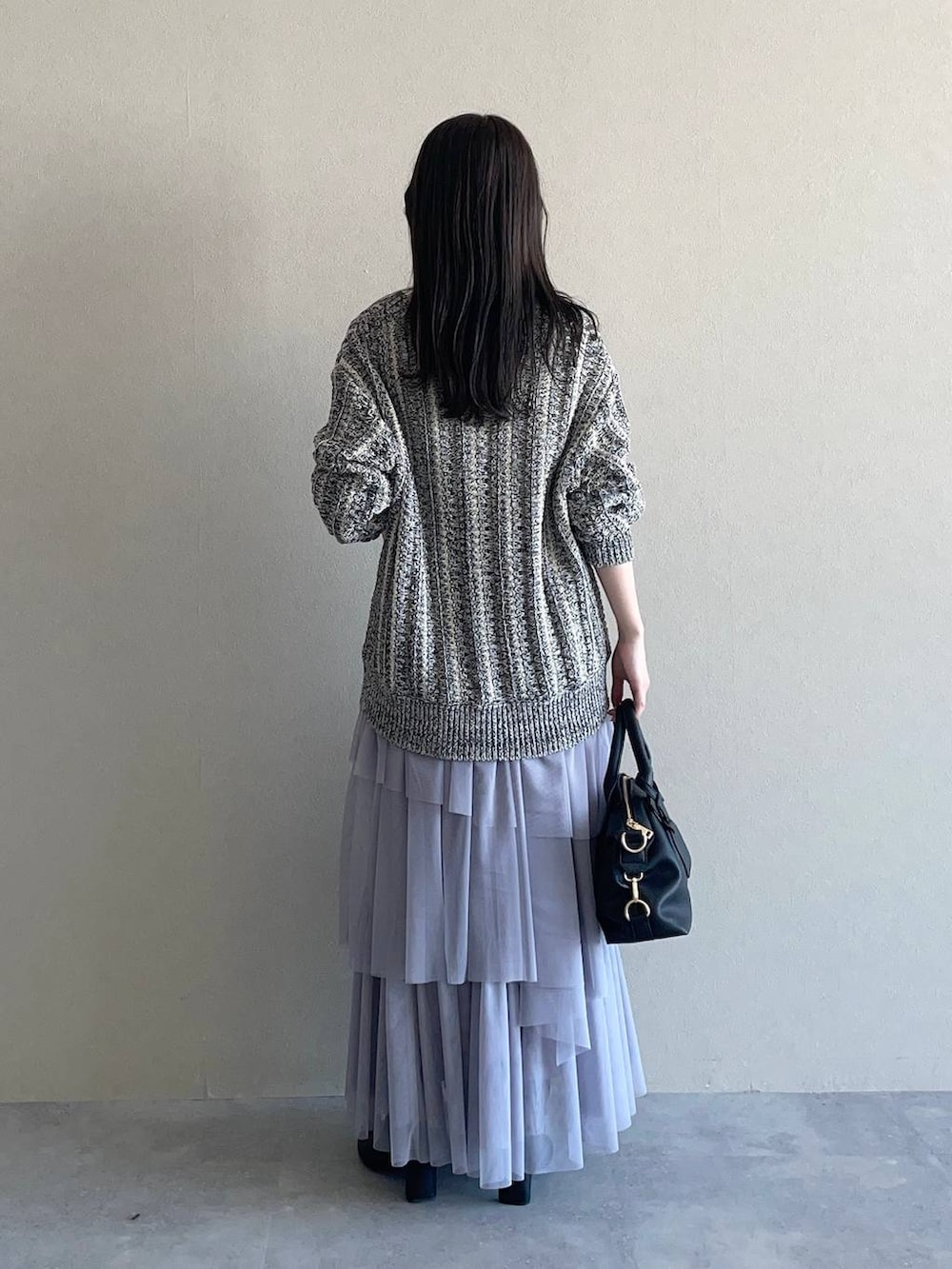 ブラック系のボストンバッグ、グレー系のスカート、ホワイト系のアンサンブルを着用したレディースの冬コーディネートの2枚目の写真