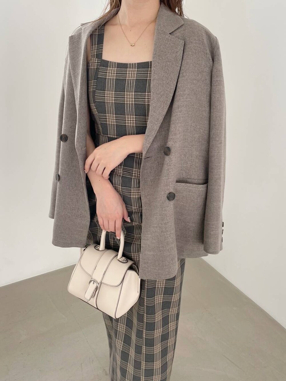 ホワイト系のハンドバッグ、ホワイト系のブーツ、グレー系のジャンパースカートを着用したレディースの秋コーディネートの4枚目の写真