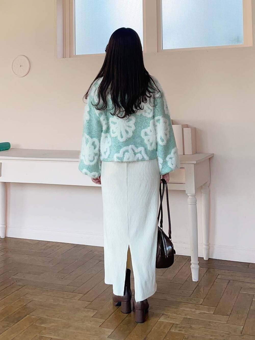 グリーン系のニット/セーター、ブラウン系のブーツ、ホワイト系のスカートを着用したレディースの冬コーディネートの2枚目の写真