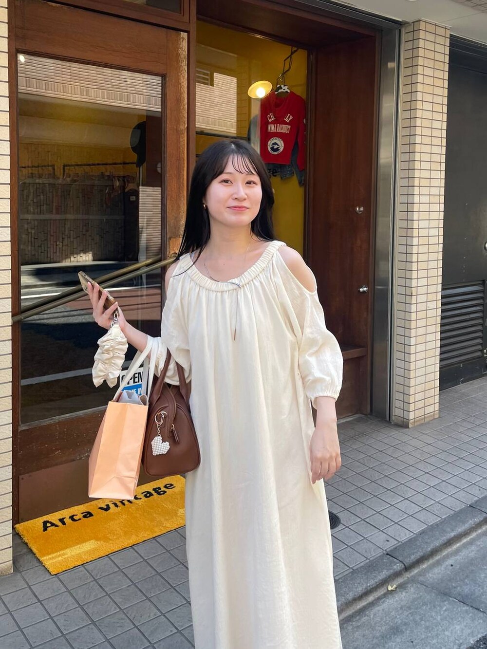 ブラウン系のショルダーバッグ、ホワイト系のワンピース、ベージュ系のキーホルダーを着用したレディースの夏コーディネートの3枚目の写真