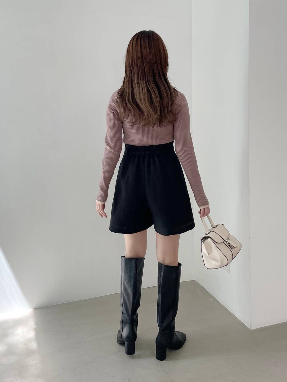 ホワイト系のハンドバッグ、ブラック系のブーツ、ブラウン系のニット/セーターを着用したレディースの秋コーディネートの2枚目の写真