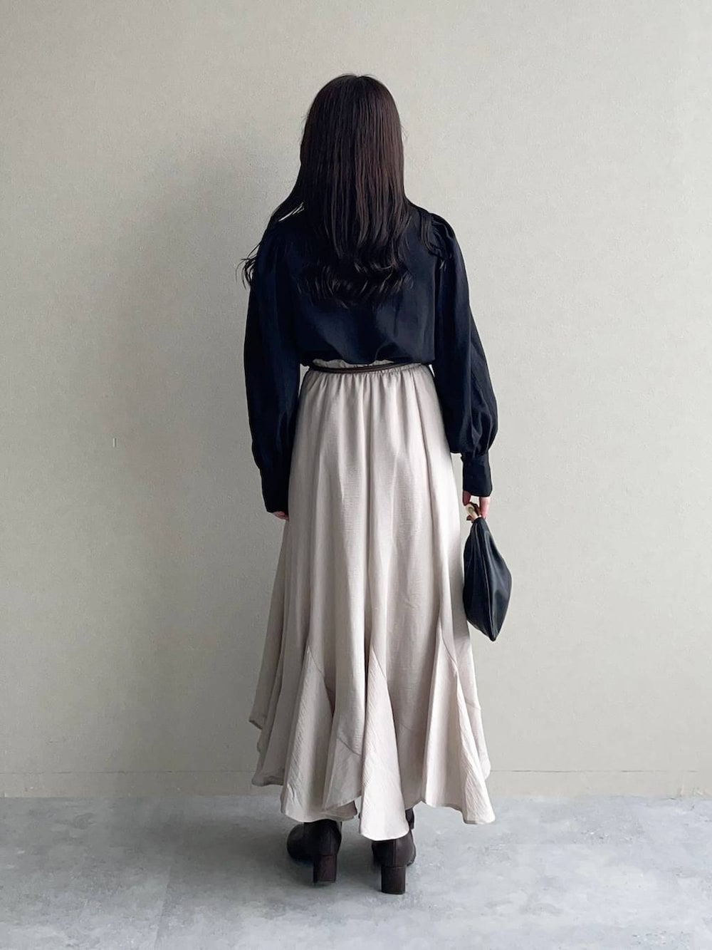 ブラック系のハンドバッグ、ブラック系のTシャツ/カットソー、ベージュ系のスカートを着用したレディースの秋コーディネートの2枚目の写真