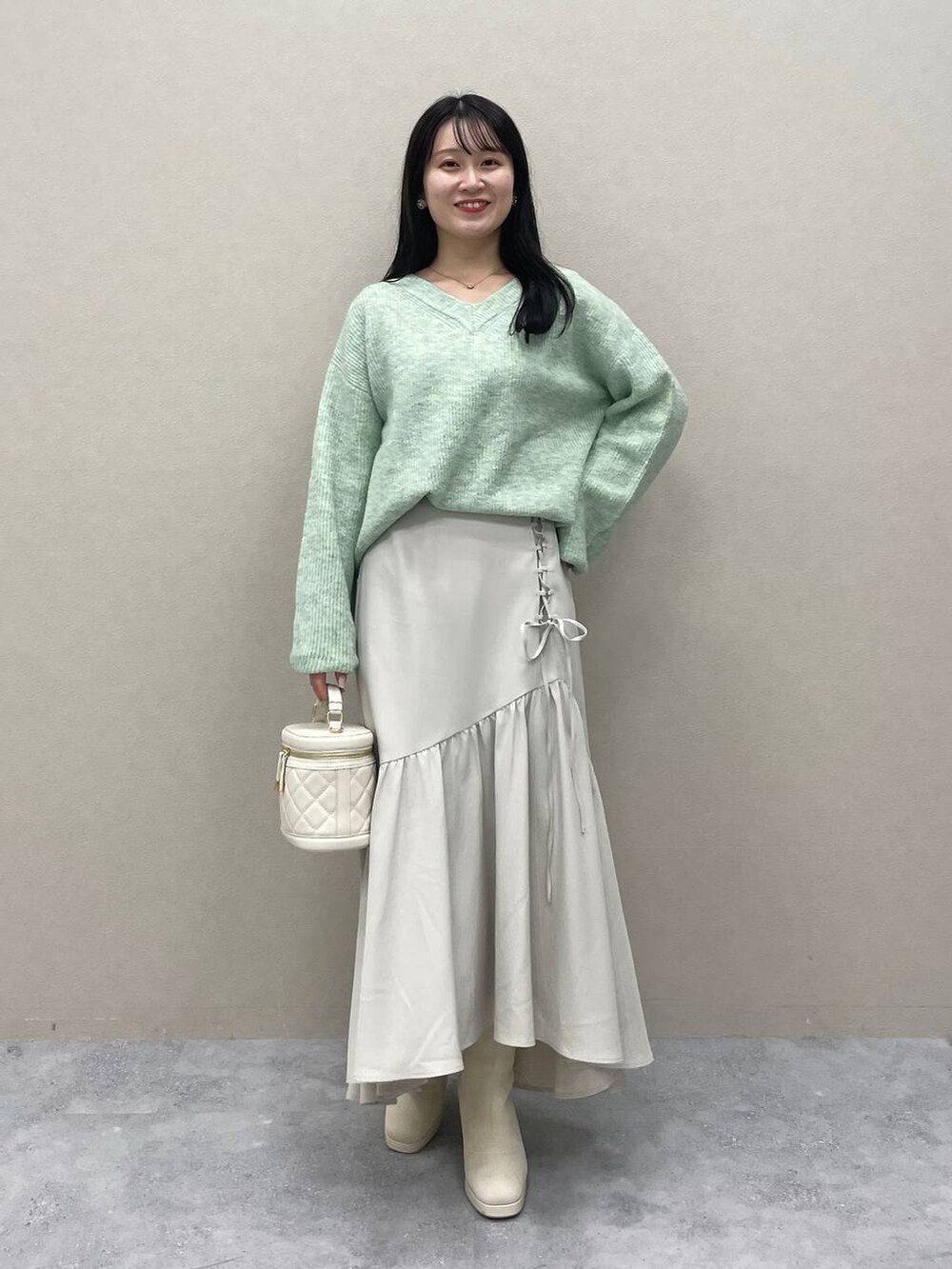 グリーン系のニット/セーター、ホワイト系のブーツ、ホワイト系のショルダーバッグを着用したレディースの冬コーディネートの2枚目の写真