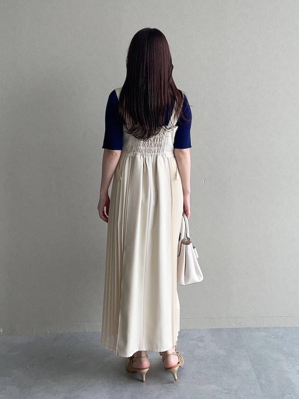 ホワイト系のショルダーバッグ、ホワイト系のジャンパースカート、ブルー系のニット/セーターを着用したレディースの春コーディネートの2枚目の写真