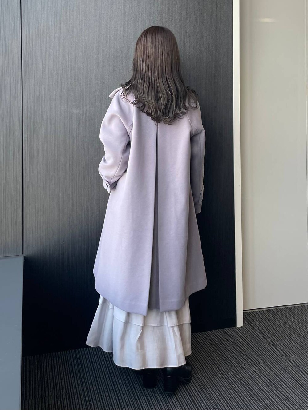 グレー系のチェスターコート、ブラック系のハンドバッグ、ブラック系のブーツを着用したレディースの秋コーディネートの2枚目の写真