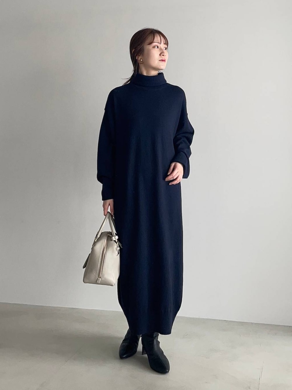 ベージュ系のハンドバッグ、ブラック系のブーツ、ブルー系のワンピースを着用したレディースの冬コーディネートの3枚目の写真