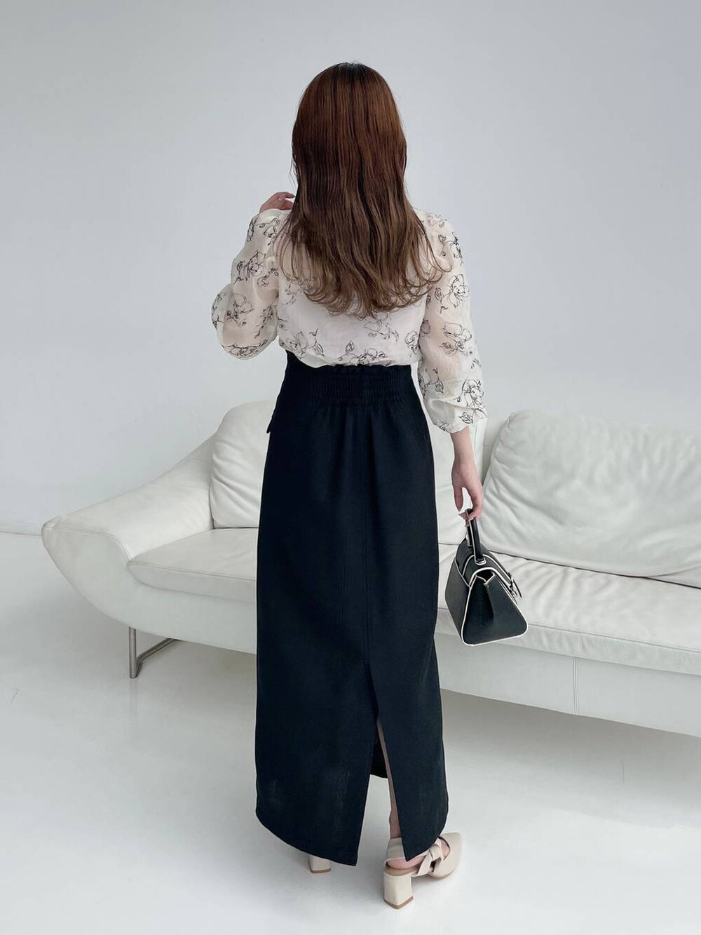 ブラック系のハンドバッグ、ホワイト系のパンプス、ブラック系のスカートを着用したレディースの秋コーディネートの2枚目の写真