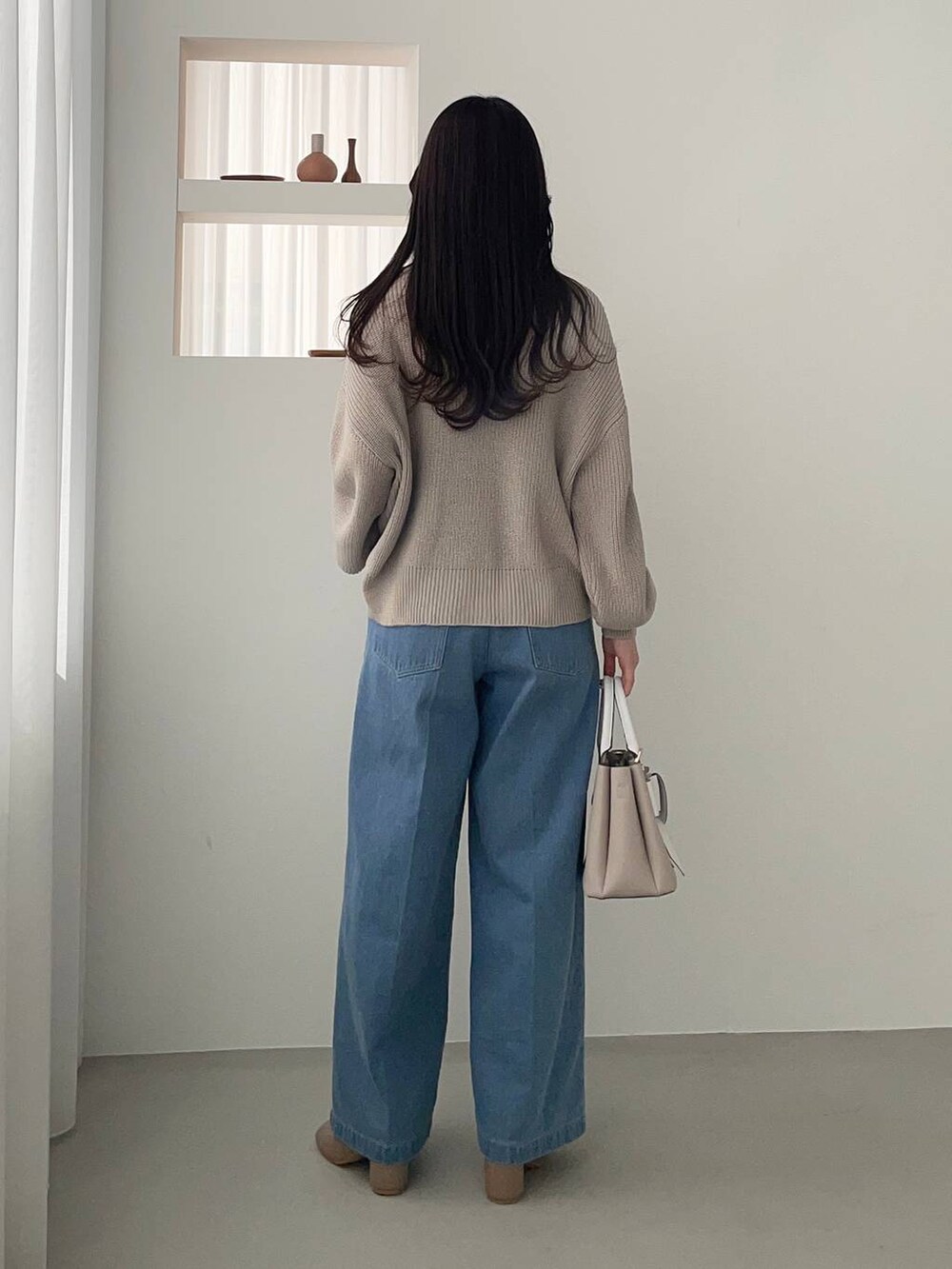 ベージュ系のショルダーバッグ、ブラウン系のパンプス、ブルー系のデニムパンツを着用したレディースの冬コーディネートの2枚目の写真