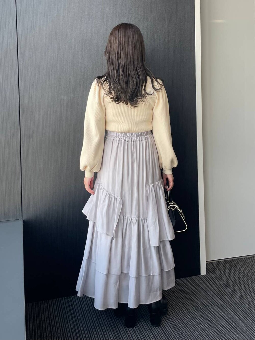 グレー系のチェスターコート、ブラック系のハンドバッグ、ブラック系のブーツを着用したレディースの秋コーディネートの4枚目の写真