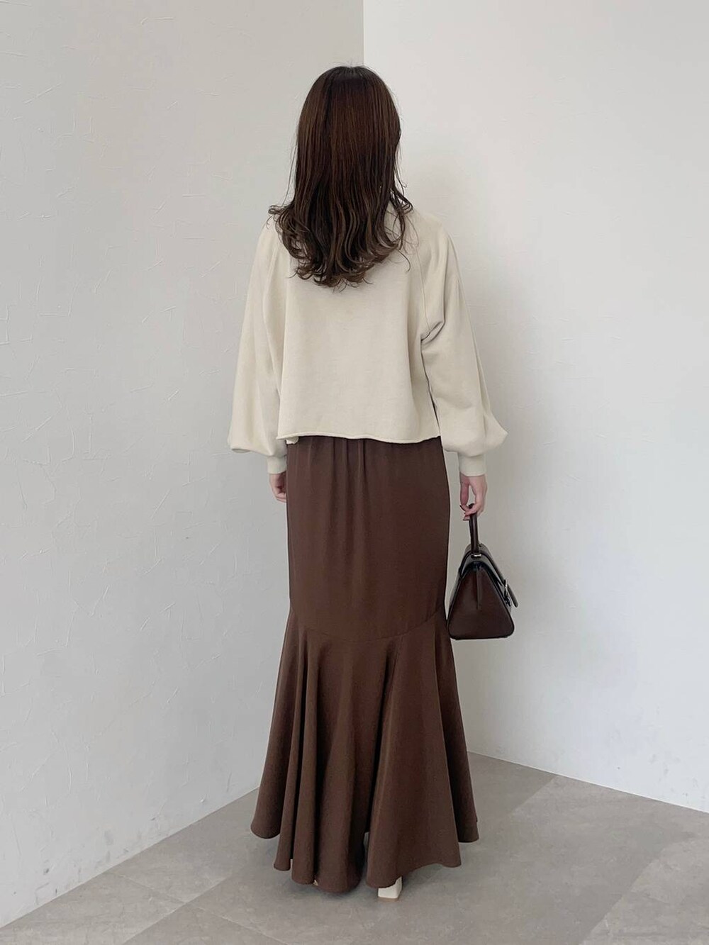 ブラウン系のハンドバッグ、ブラウン系のスカート、ホワイト系のパンプスを着用したレディースの秋コーディネートの2枚目の写真