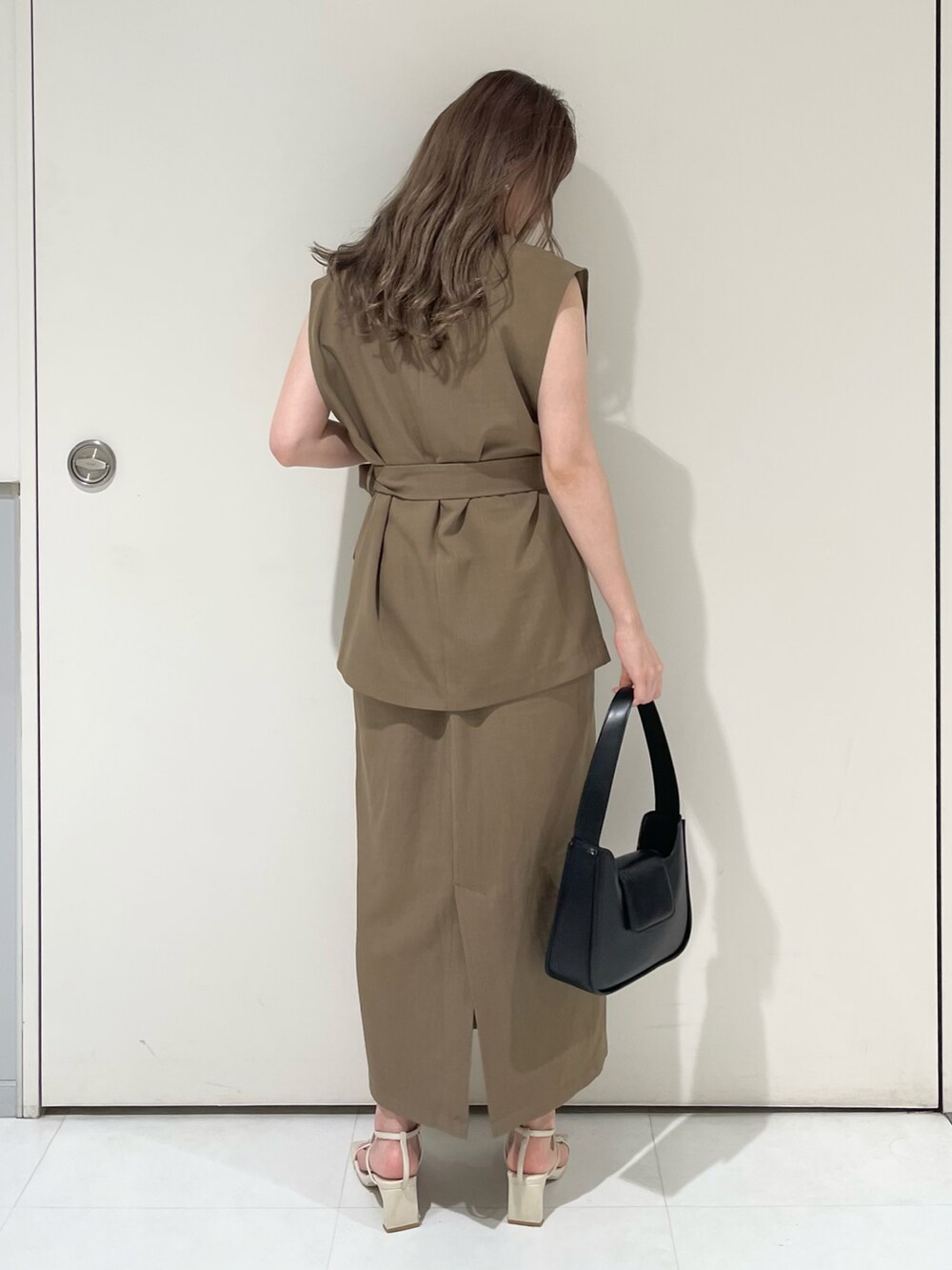 ブラウン系のベスト、ブラウン系のスカート、ブラック系のハンドバッグを着用したレディースの夏コーディネートの2枚目の写真