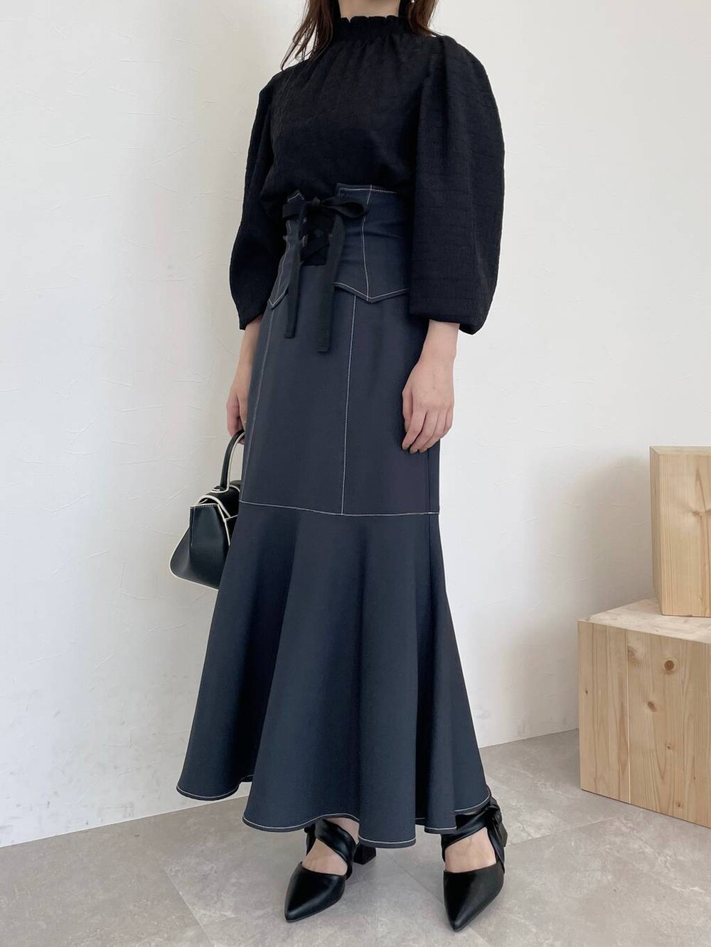 ブラック系のハンドバッグ、グレー系のスカート、ブラック系のパンプスを着用したレディースの夏コーディネートの4枚目の写真