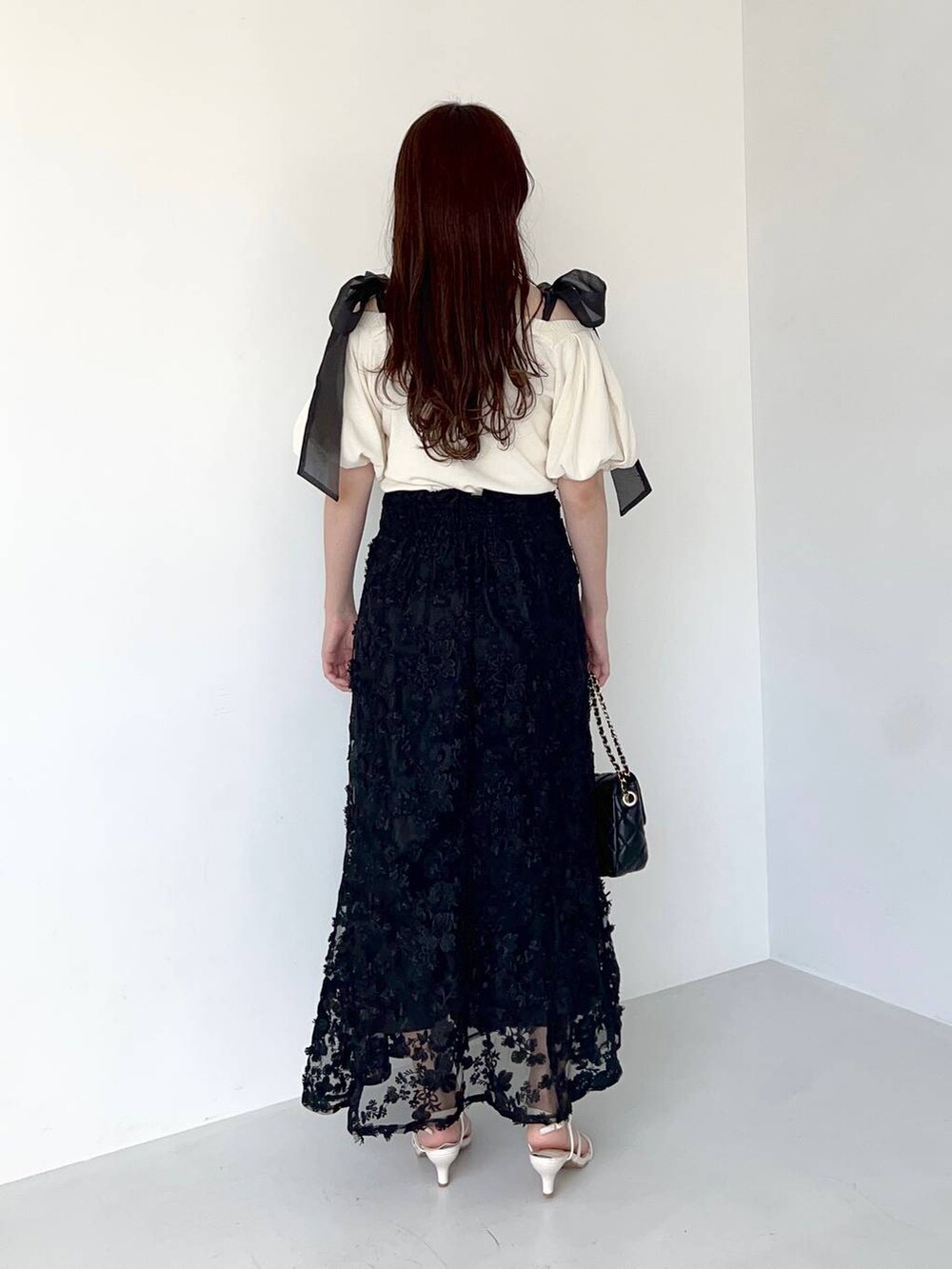 ホワイト系のニット/セーター、ブラック系のショルダーバッグ、ホワイト系のサンダルを着用したレディースの夏コーディネートの2枚目の写真