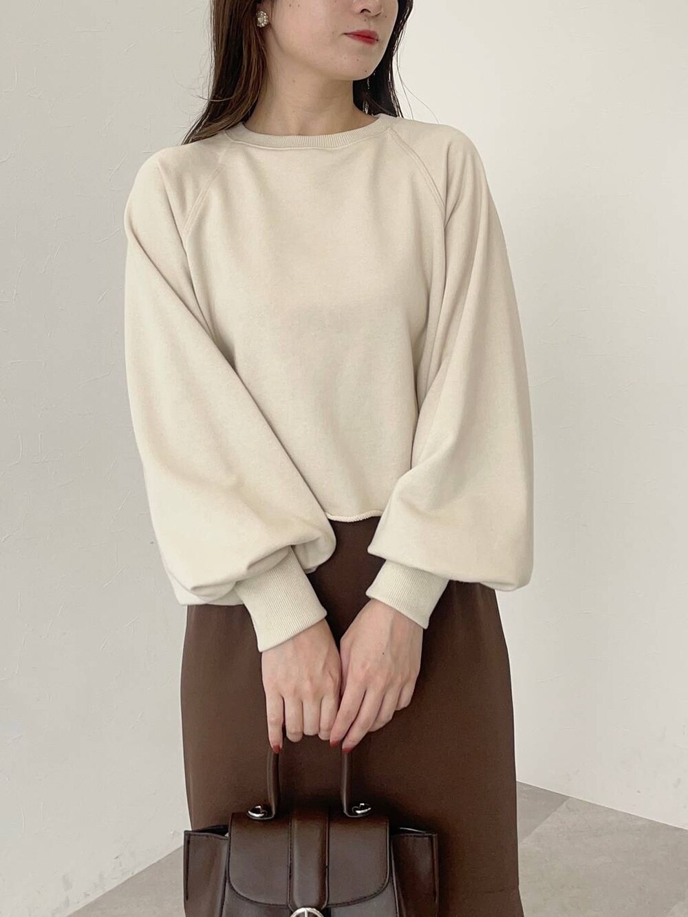 ブラウン系のハンドバッグ、ブラウン系のスカート、ホワイト系のパンプスを着用したレディースの秋コーディネートの3枚目の写真