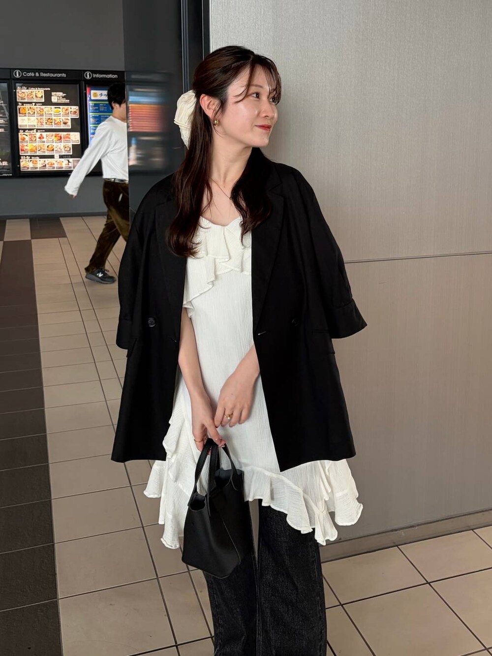 ブラック系のデニムパンツ、ブラック系のサンダル、ホワイト系のチュニックを着用したレディースの春コーディネートの3枚目の写真