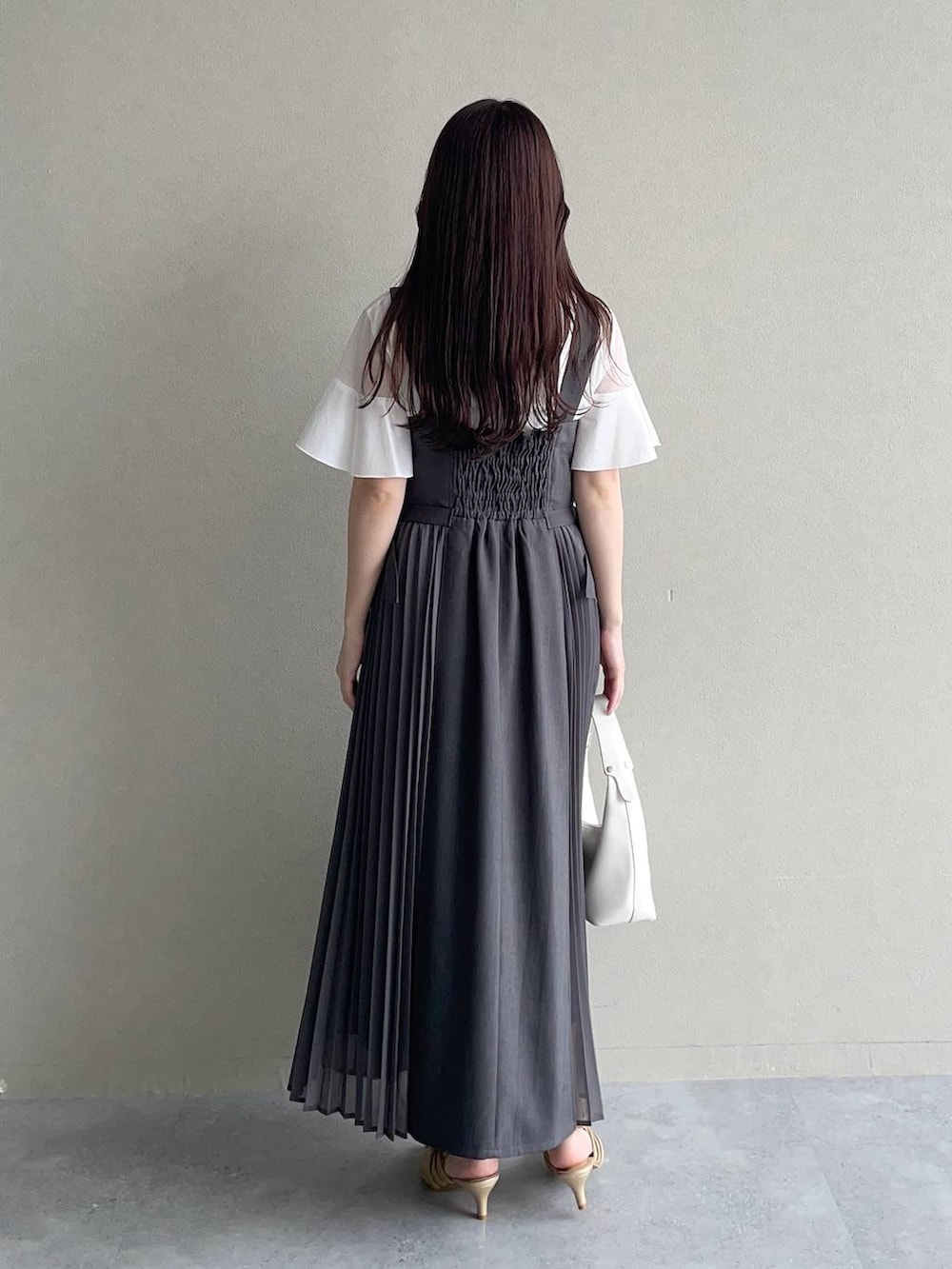 グレー系のジャンパースカート、ホワイト系のTシャツ/カットソー、ホワイト系のショルダーバッグを着用したレディースの春コーディネートの2枚目の写真