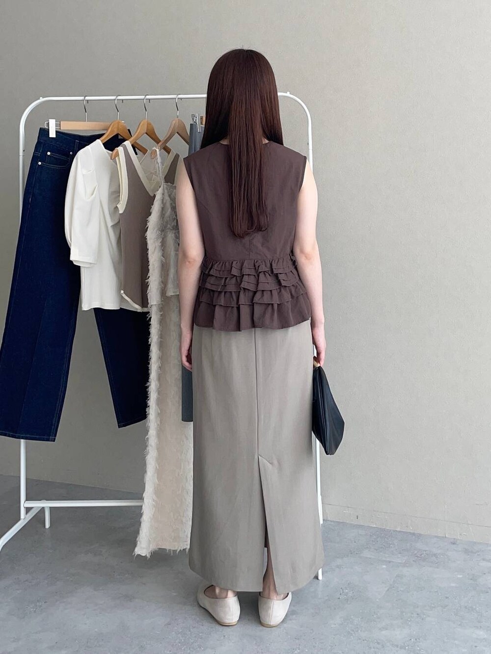 ブラック系のハンドバッグ、ブラウン系のベスト、ベージュ系のスカートを着用したレディースの夏コーディネートの2枚目の写真