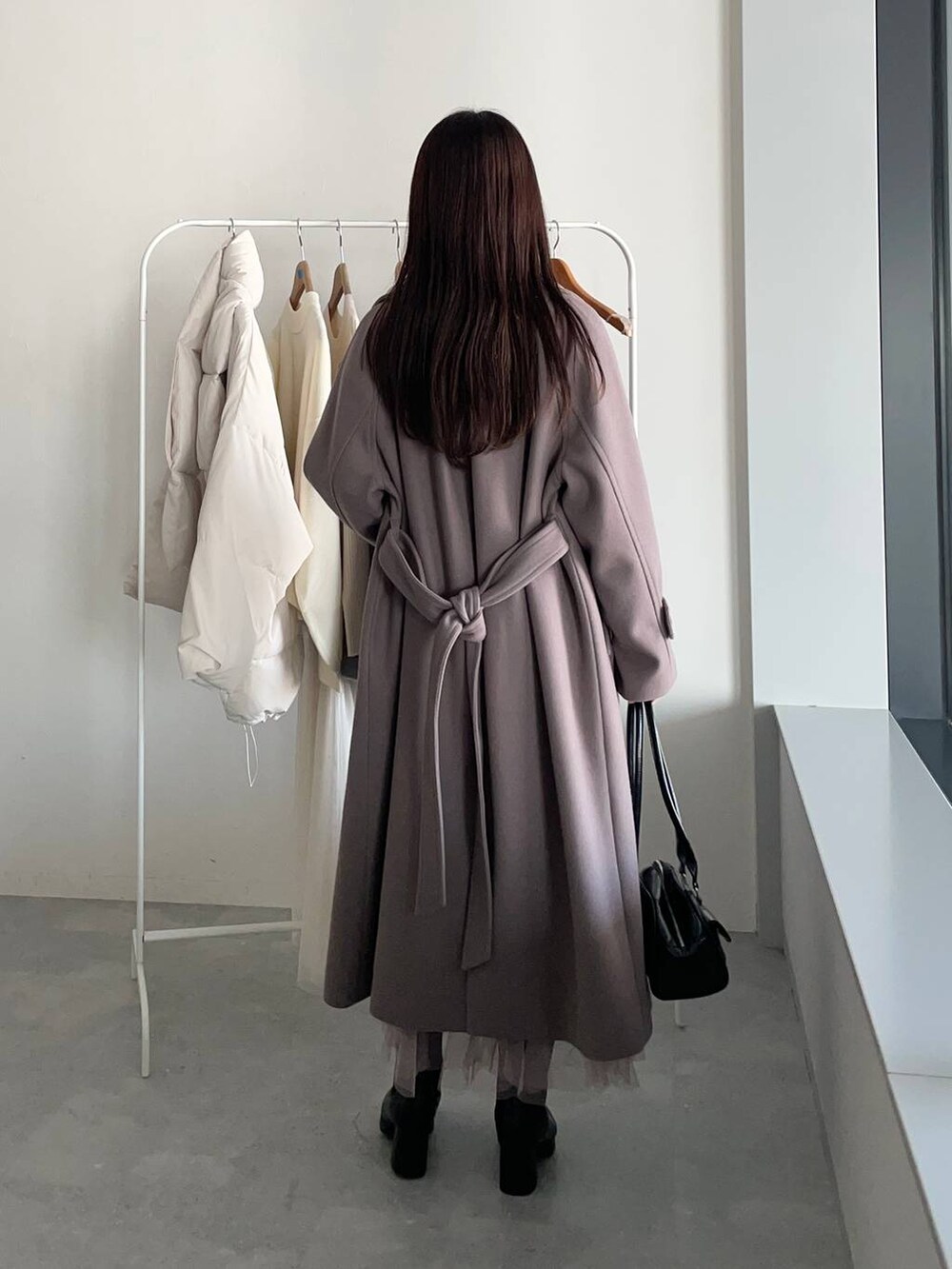 ブラウン系のチェスターコート、ブラック系のブーツ、ホワイト系のワンピースを着用したレディースの冬コーディネートの2枚目の写真