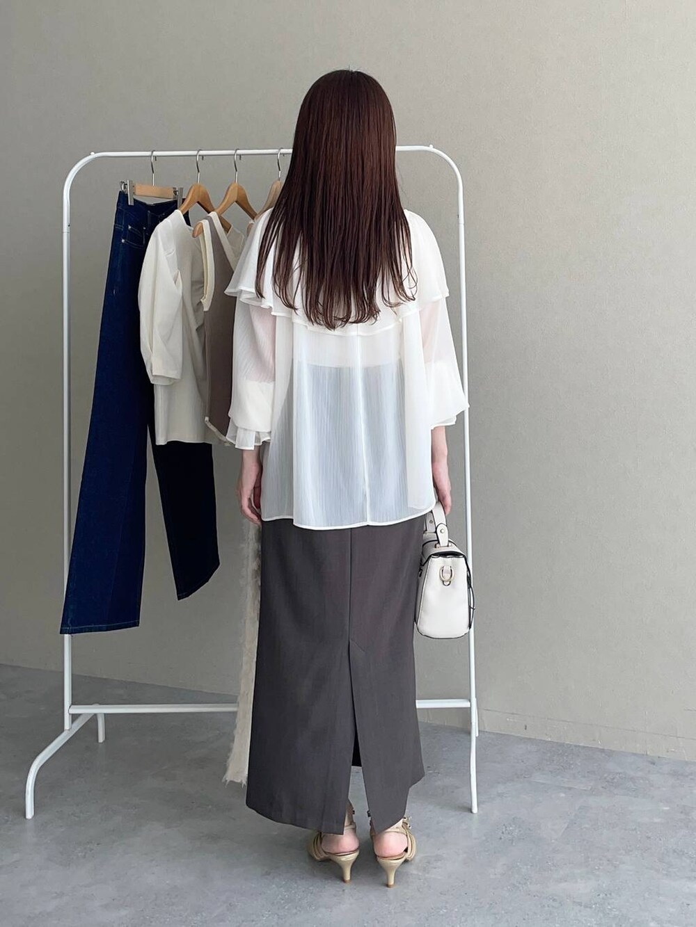 ゴールド系のパンプス、ホワイト系のショルダーバッグ、グレー系のスカートを着用したレディースの秋コーディネートの2枚目の写真