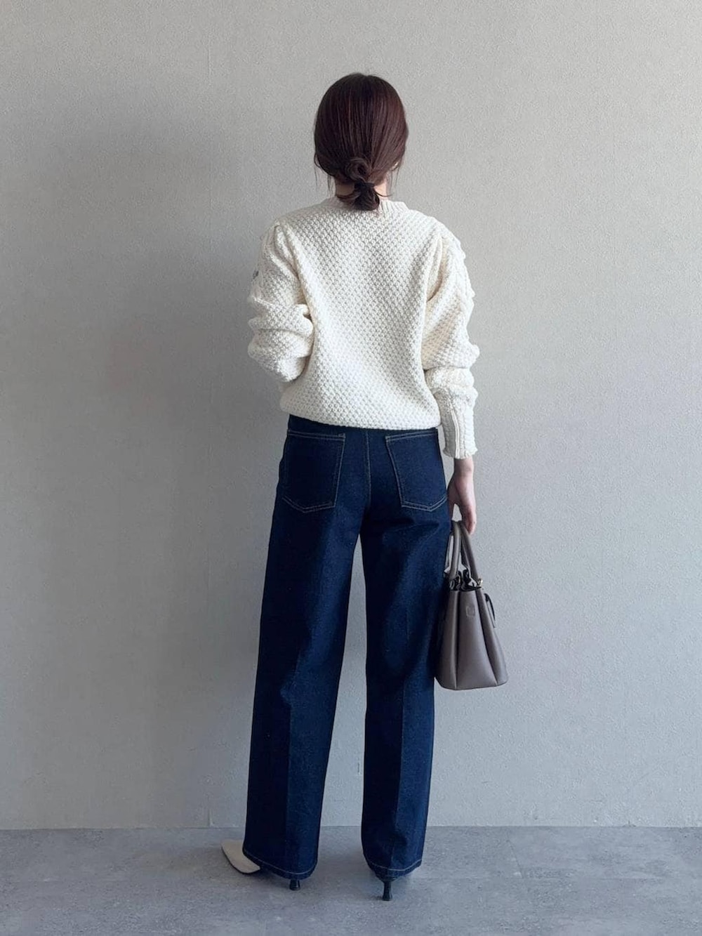 ベージュ系のショルダーバッグ、ブルー系のデニムパンツ、ホワイト系のニット/セーターを着用したレディースの冬コーディネートの2枚目の写真