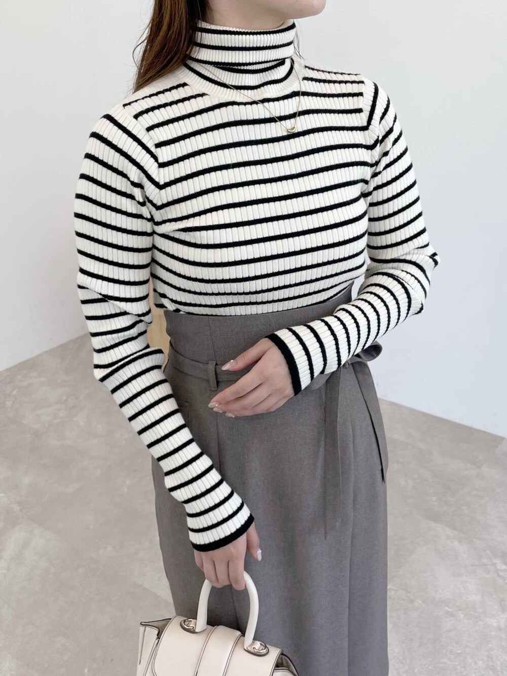 ブラウン系のスカート、ホワイト系のハンドバッグ、ブラック系のブーツを着用したレディースの秋コーディネートの3枚目の写真