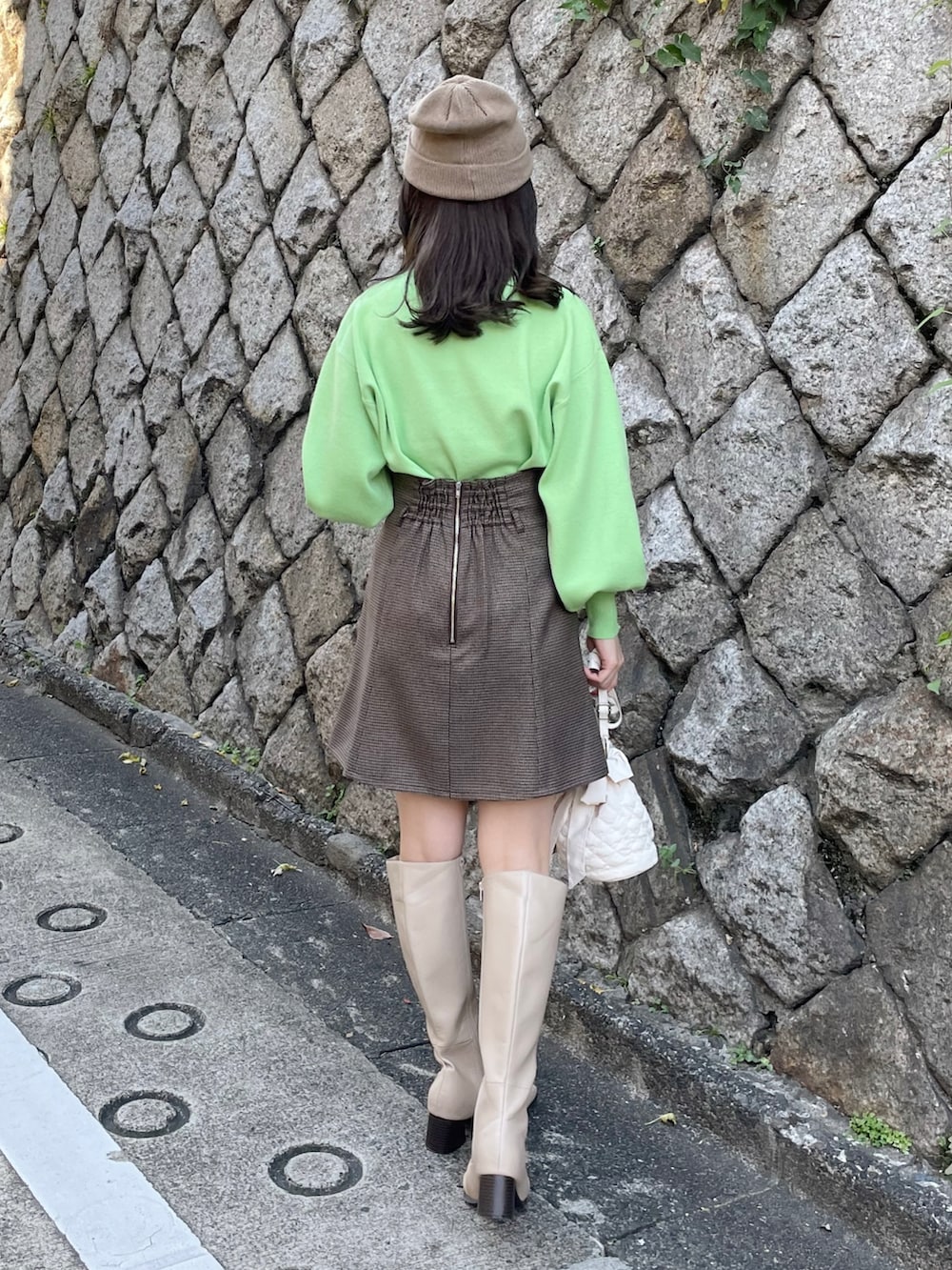 グリーン系のニット/セーター、ブラウン系のスカート、ベージュ系のブーツを着用したレディースの秋コーディネートの2枚目の写真