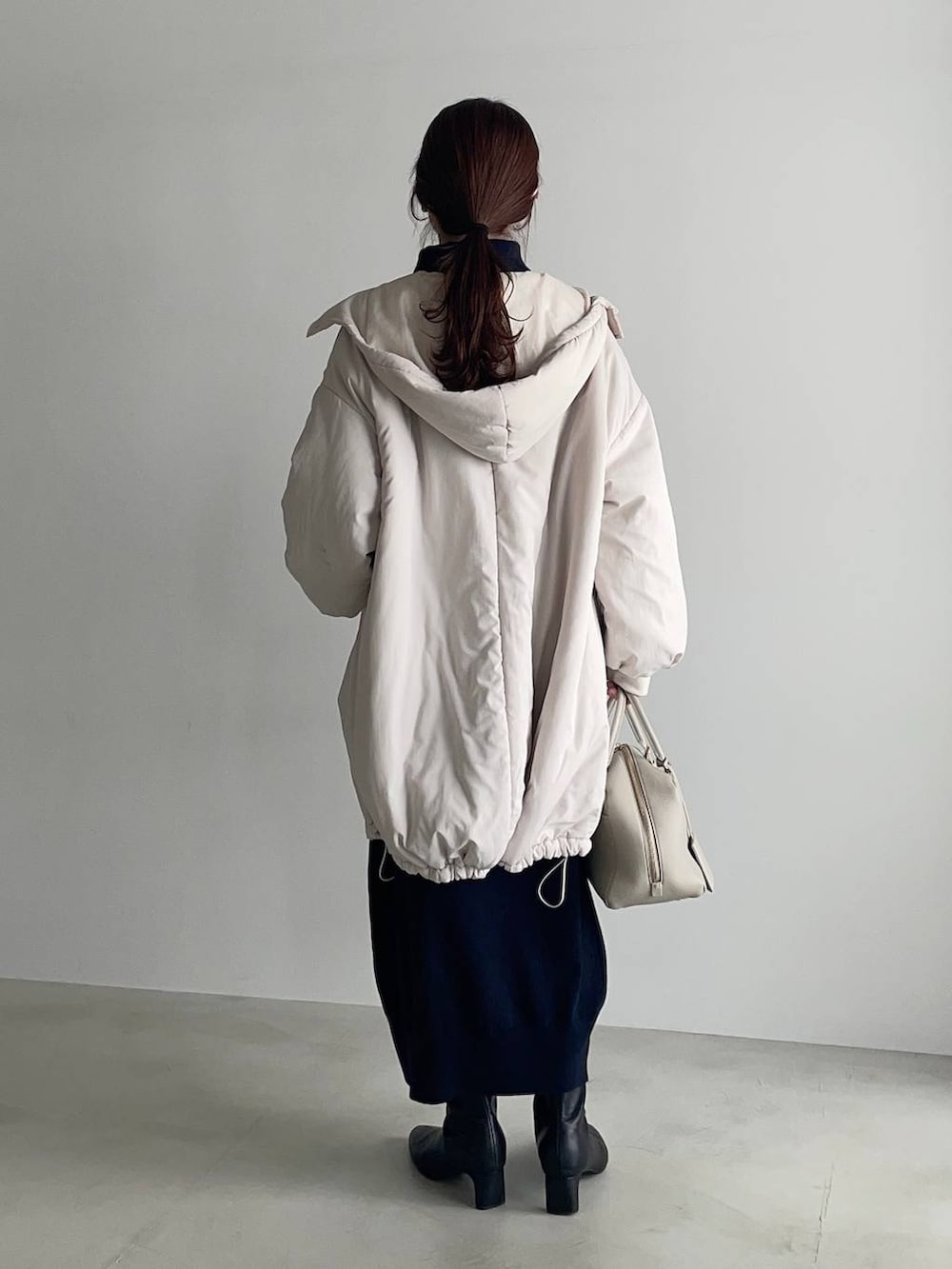 ベージュ系のハンドバッグ、ブラック系のブーツ、ブルー系のワンピースを着用したレディースの冬コーディネートの2枚目の写真