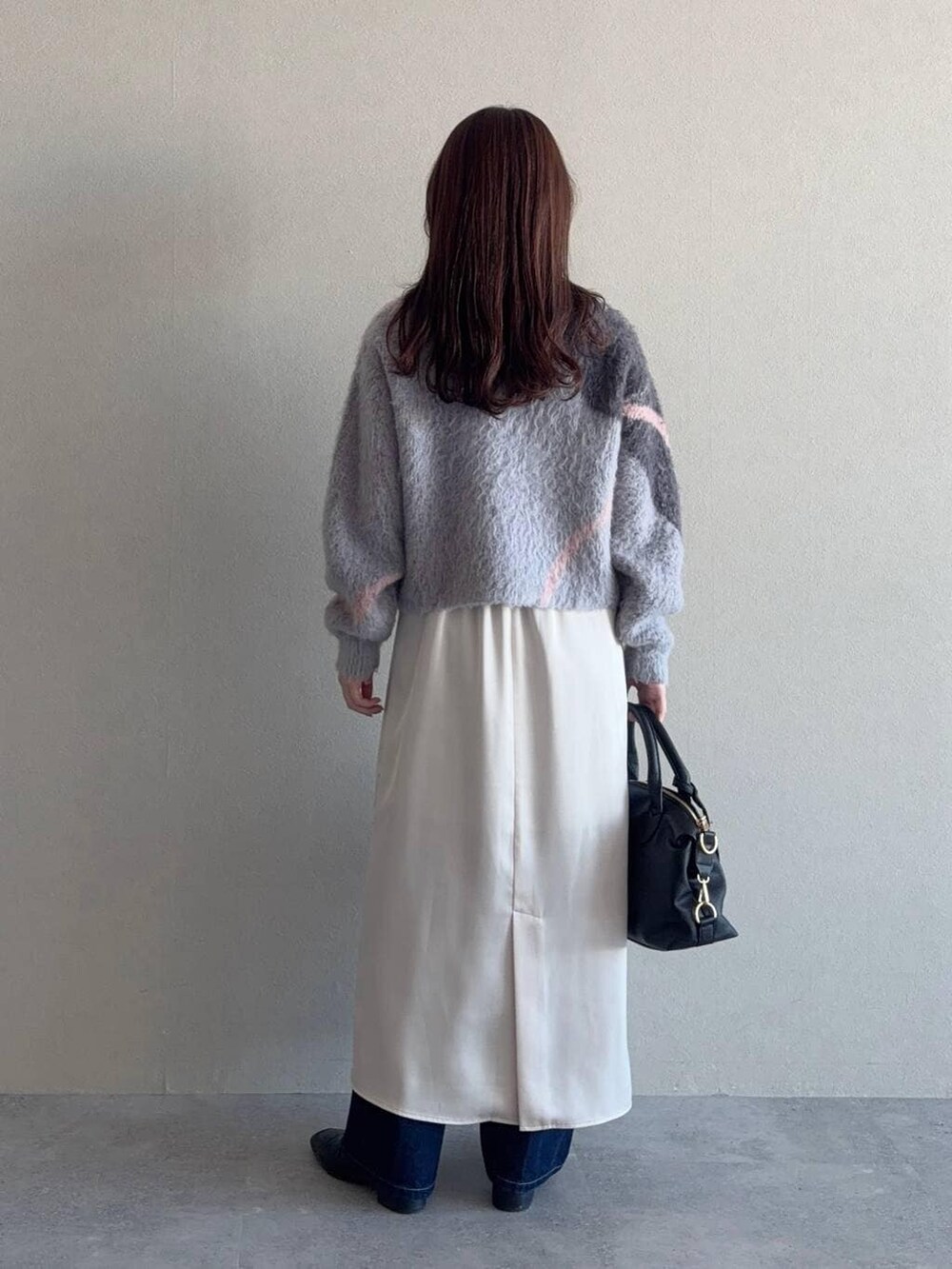 グレー系のニット/セーター、ブラック系のボストンバッグ、ブルー系のデニムパンツを着用したレディースの冬コーディネートの2枚目の写真