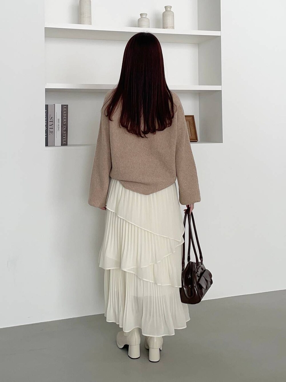 ホワイト系のブーツ、ベージュ系のニット/セーター、ブラウン系のハンドバッグを着用したレディースの冬コーディネートの2枚目の写真