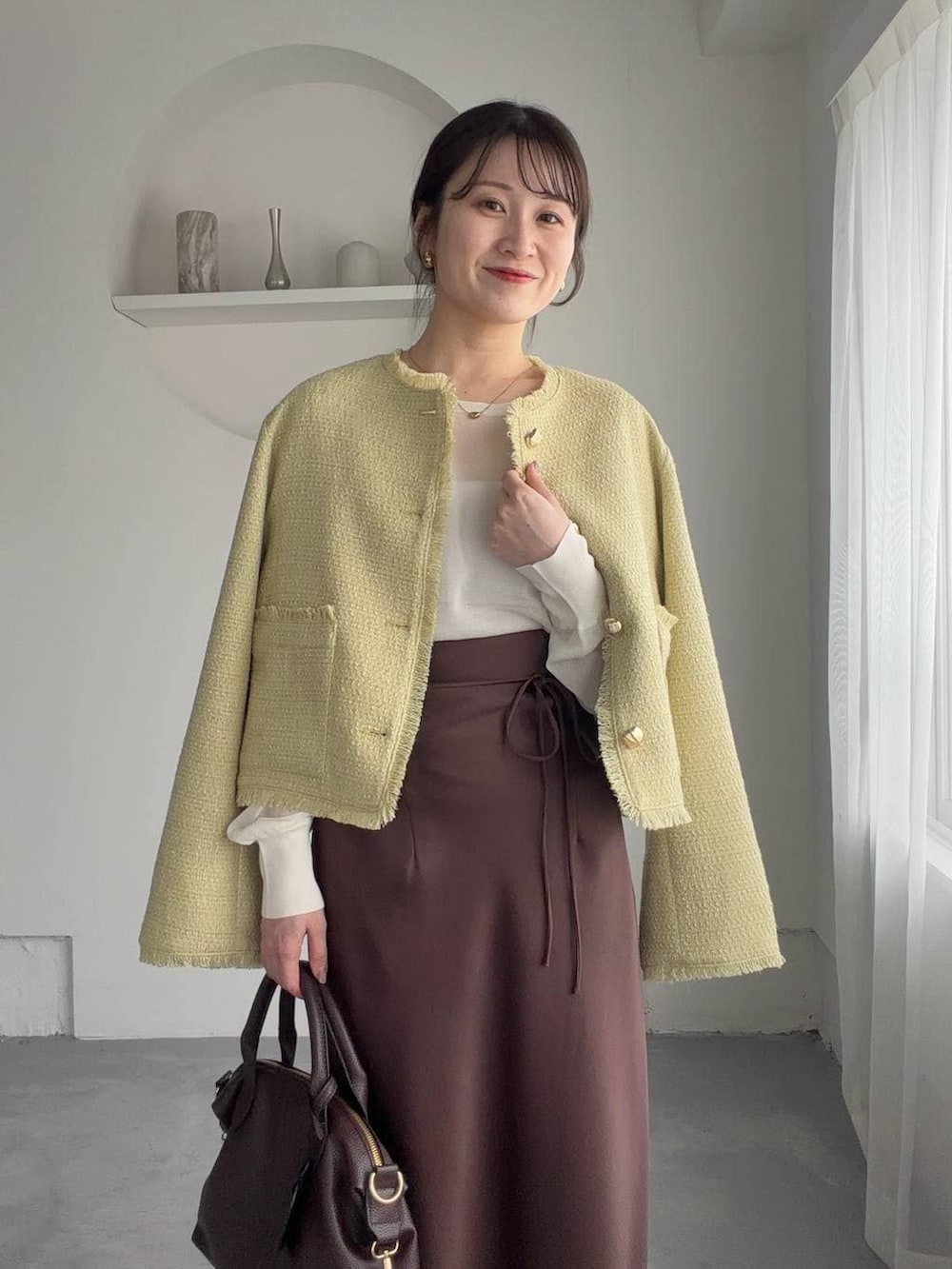 ブラウン系のボストンバッグ、ブラウン系のサンダル、イエロー系のノーカラージャケットを着用したレディースの春コーディネートの3枚目の写真