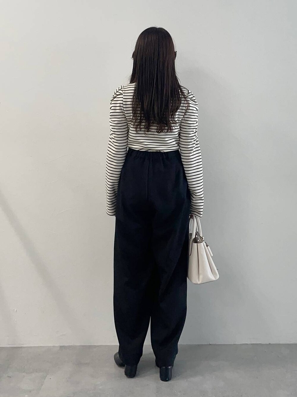 ホワイト系のショルダーバッグ、ブラック系のパンプス、ブラック系のスラックスを着用したレディースの春コーディネートの2枚目の写真