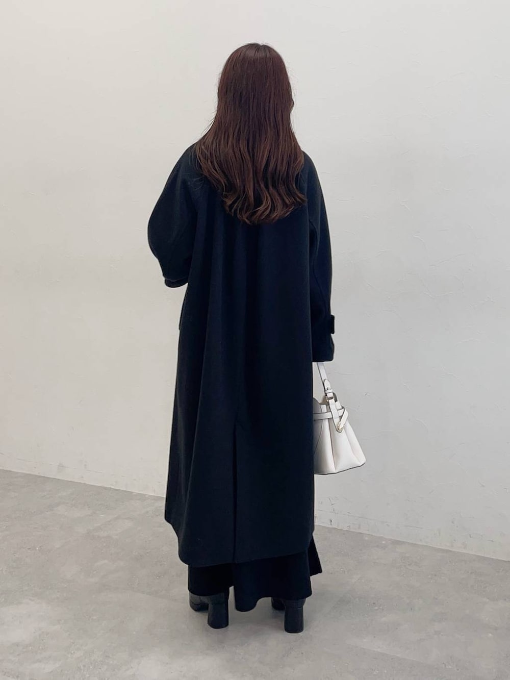 ブラック系のチェスターコート、ブラック系のワンピース、ホワイト系のショルダーバッグを着用したレディースの秋コーディネートの2枚目の写真