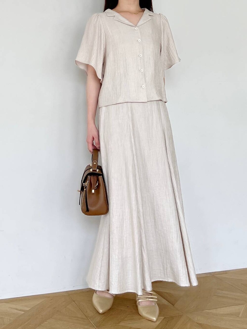 ゴールド系のパンプス、ブラウン系のショルダーバッグ、ベージュ系のスカートを着用したレディースの夏コーディネートの4枚目の写真