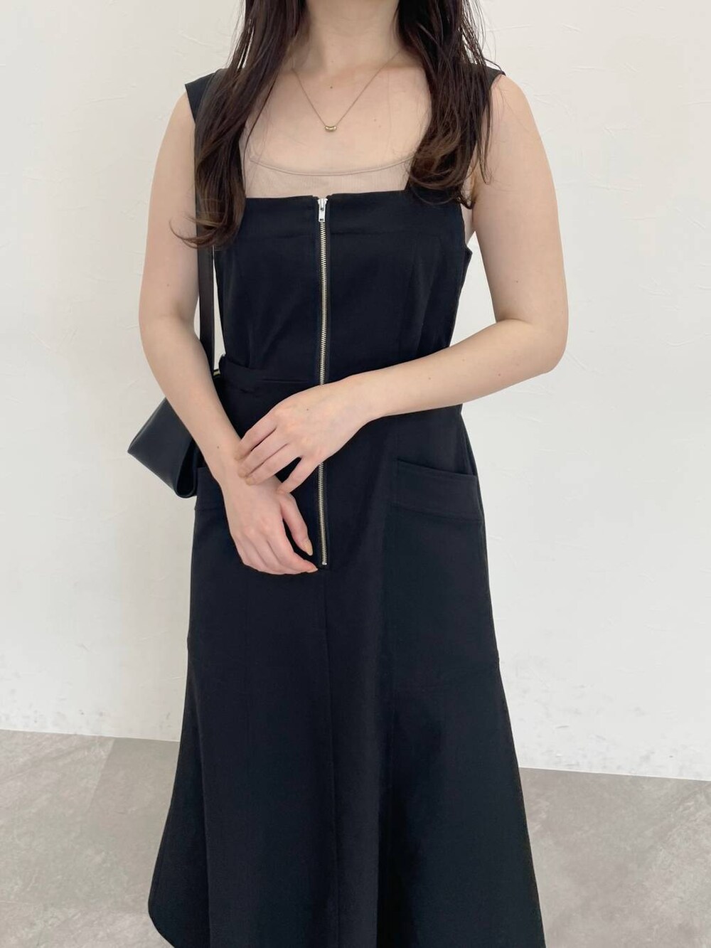 ブラック系のジャンパースカート、ブラック系のショルダーバッグ、ホワイト系のサンダルを着用したレディースの春コーディネートの3枚目の写真