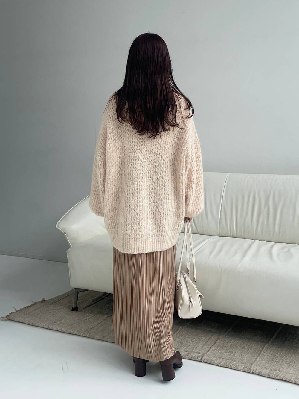 ベージュ系のスカート、ブラウン系のブーツ、ホワイト系のハンドバッグを着用したレディースの冬コーディネートの2枚目の写真