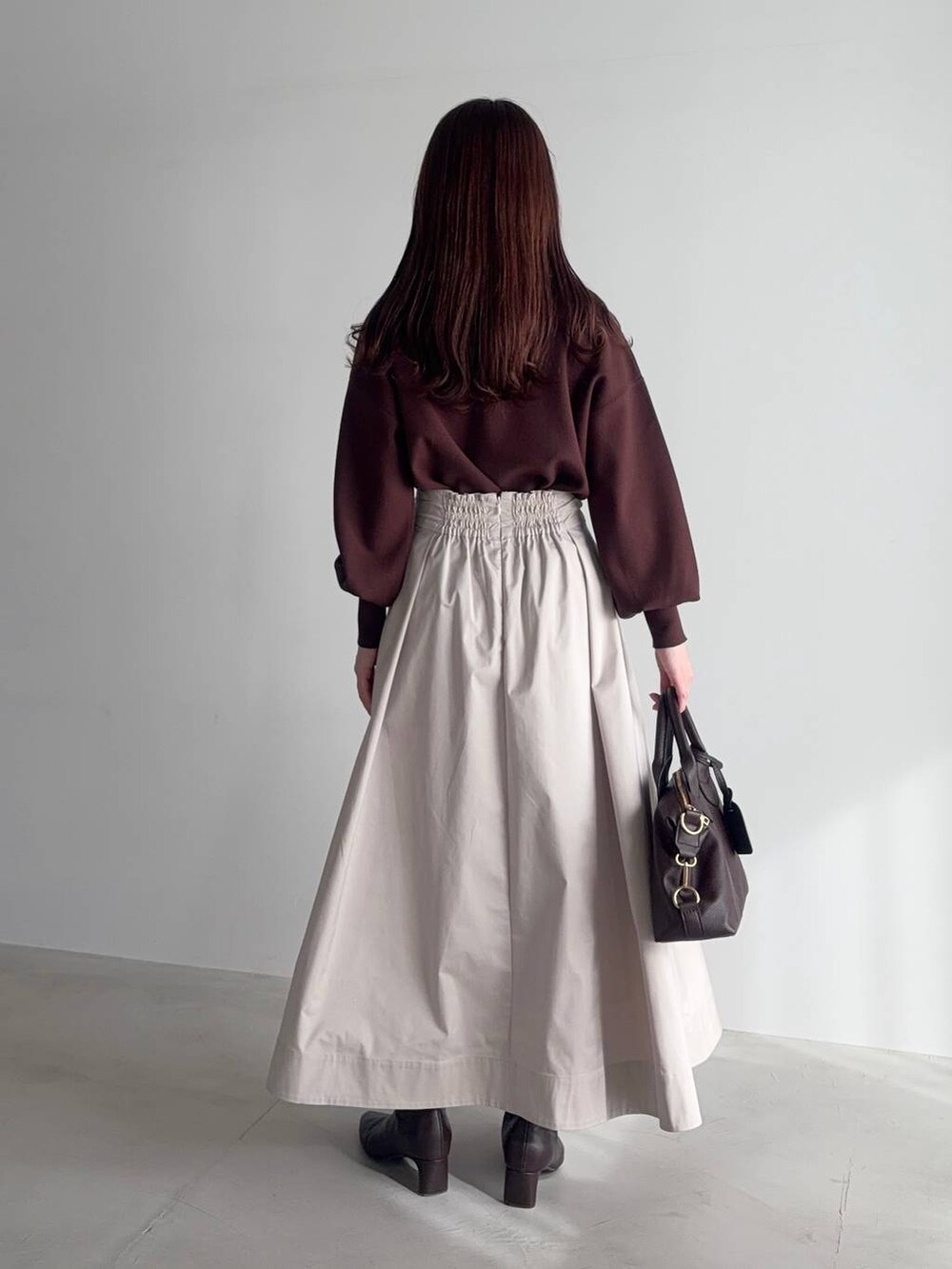 ブラウン系のボストンバッグ、ブラウン系のブーツ、ベージュ系のスカートを着用したレディースの冬コーディネートの2枚目の写真